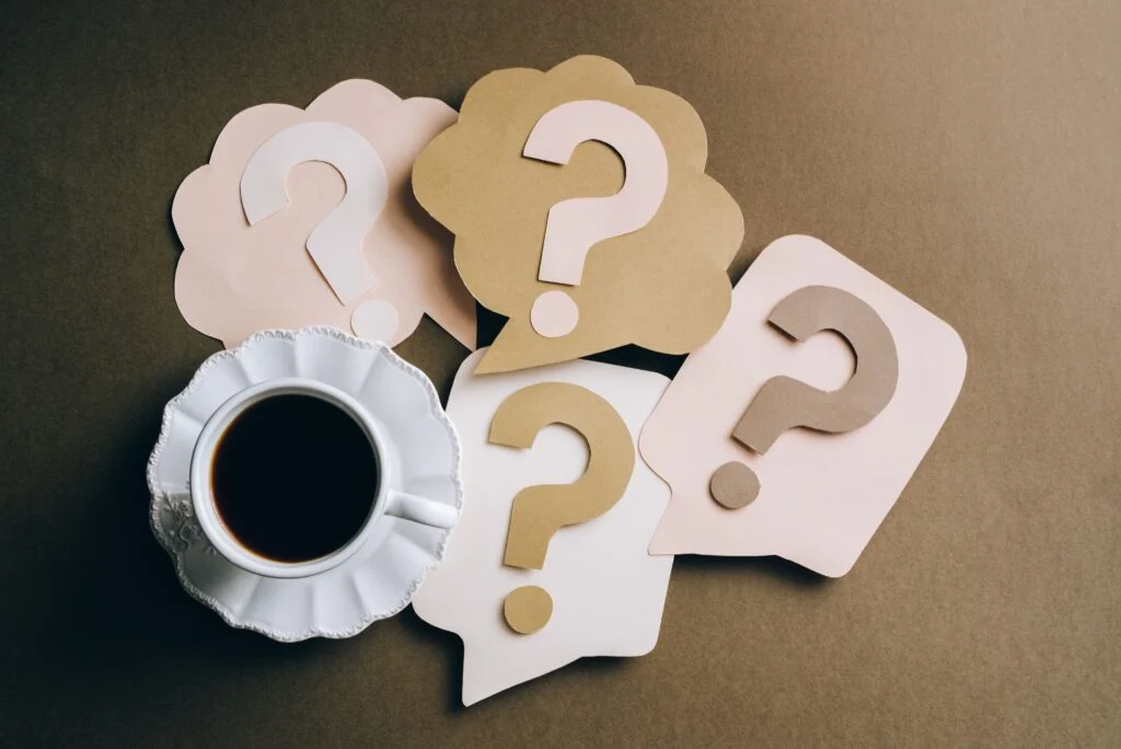 Cup of coffee next to paper speech bubbles with question marks