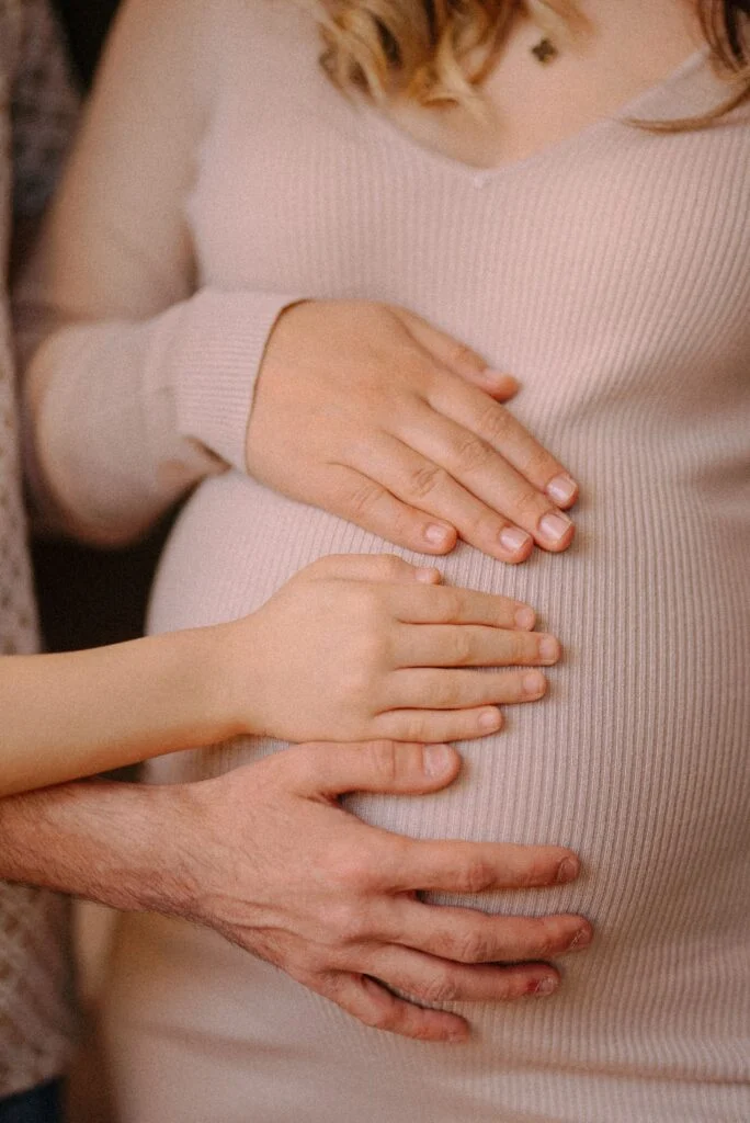 A pregnant woman with her own, a child's and a partner's hands resting on her bump