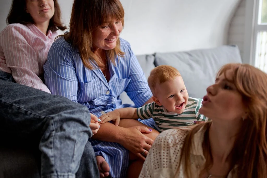 Moms chatting on a sofa while a toddler laughs